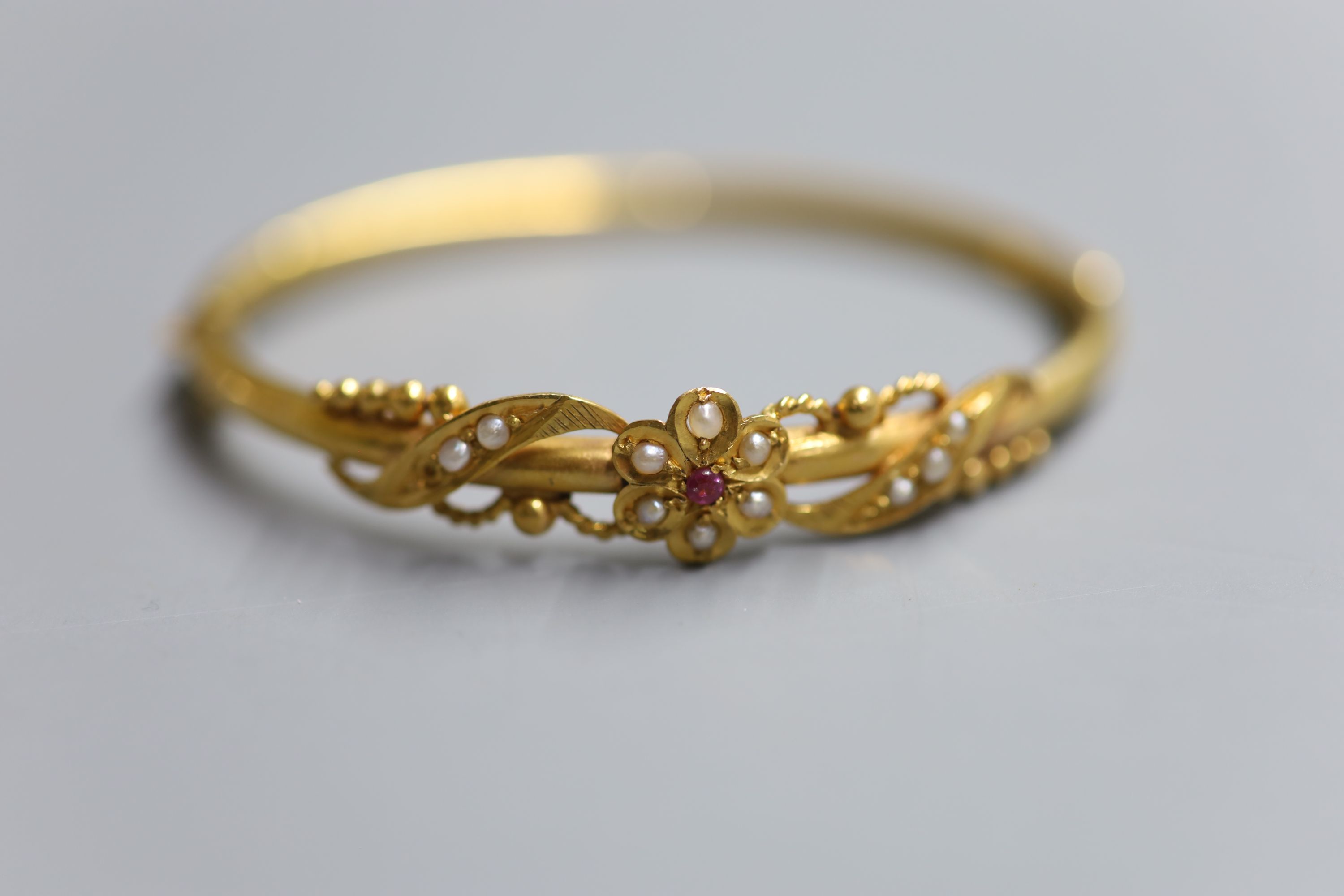 A late Victorian yellow metal, ruby and seed pearl set hinged bangle, gross 10.6 grams.